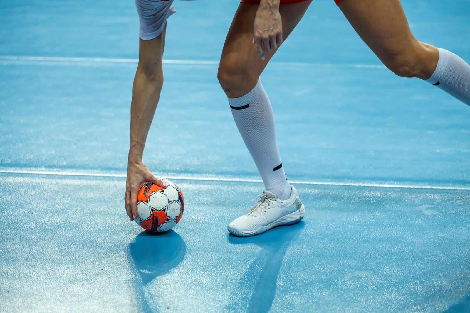 Handballspielerin legt die Hand auf den Ball am Hallenboden